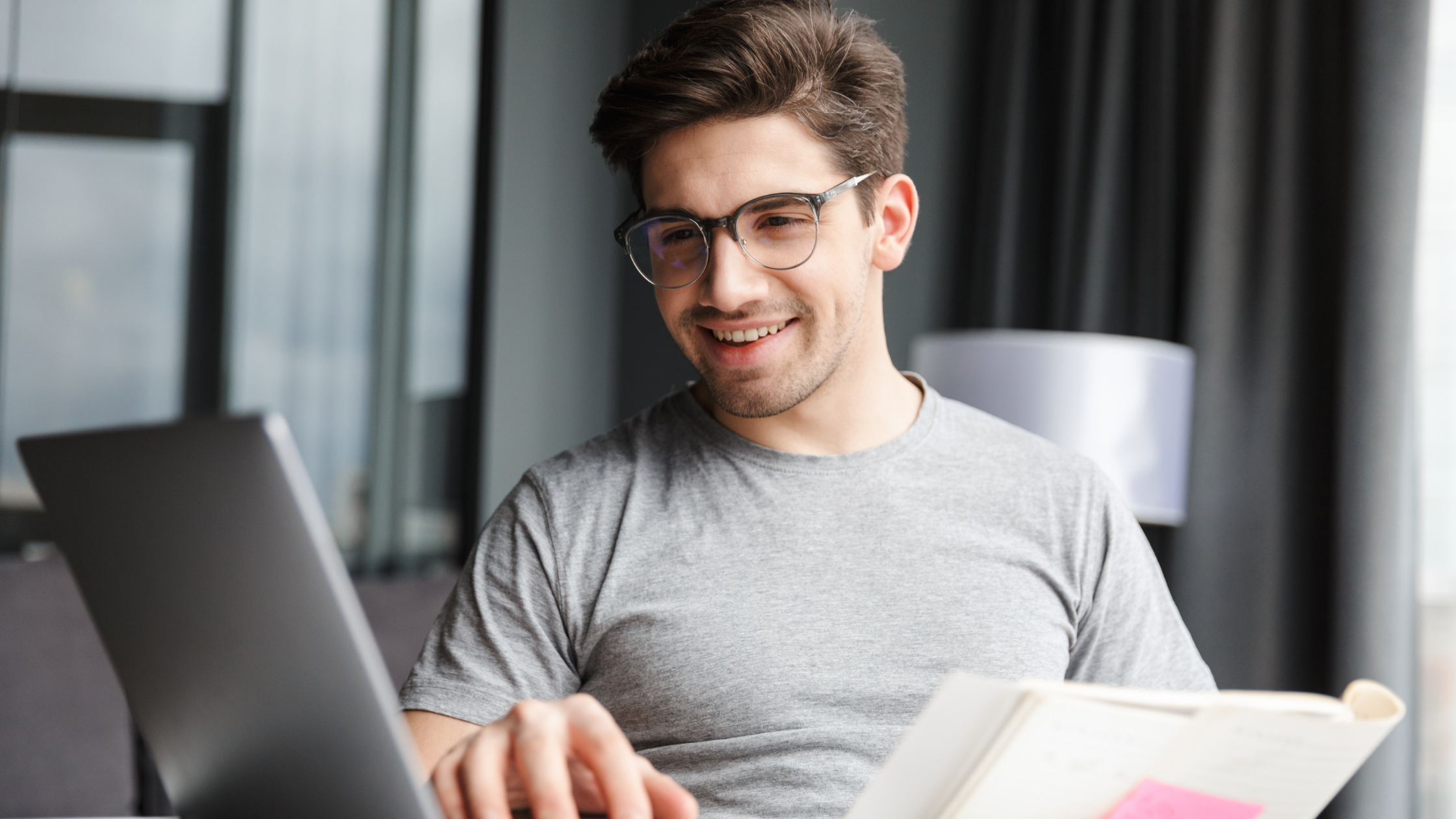chico con gafas, mirando el ordenador y un cuaderno